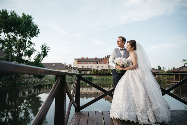 The bride and groom stand on the bridge and look away