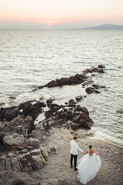 Foto gratuita la sposa e lo sposo camminano verso il tramonto sul mare