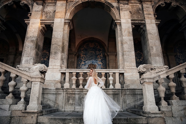 Невеста в пол оборота стоит на лестнице старинного здания