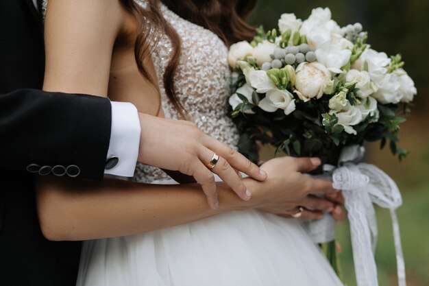 Bride holds a beautiful bouquet and groom hugs her for back