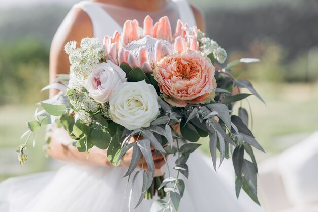 Bride holds the beautiful bridal bouquet with roses, eucalyptus and giant protea