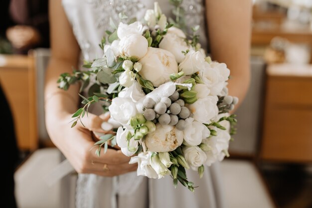 花嫁は白牡丹と緑の装飾が施された美しいブライダルブーケを持っています