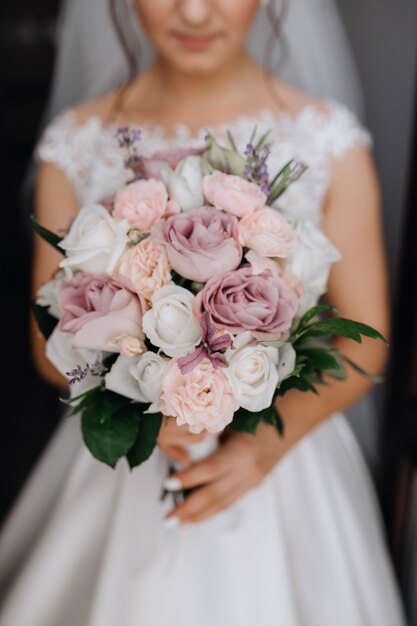 花嫁は白、紫、ピンクのバラで美しいブライダルブーケを保持しています。