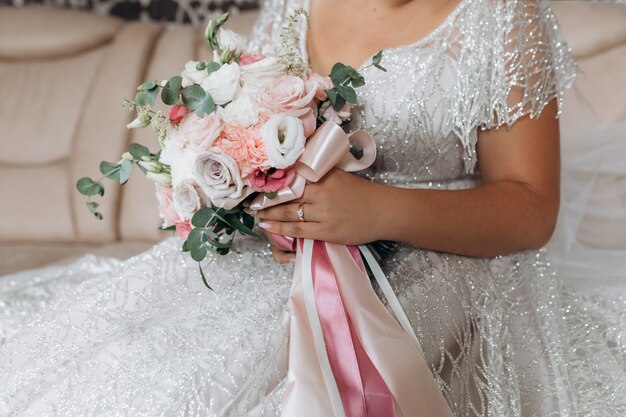 Bride holds the bridal bouquet with white and pink roses and other floral decor