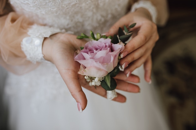 Bride holds a butonholle with pink rose