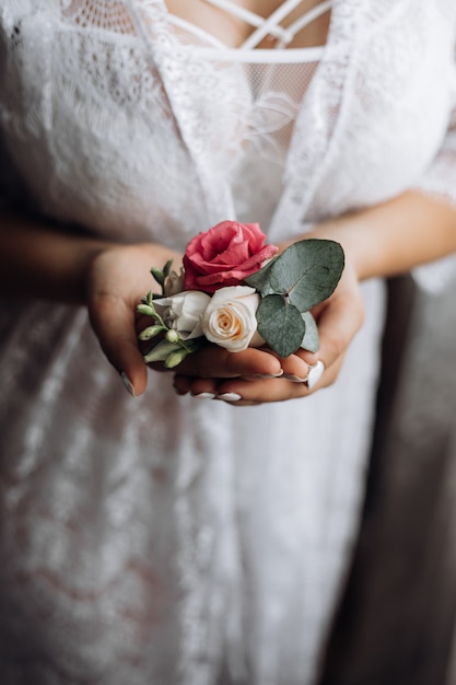 Bride holds a butonholle with pink and white roses