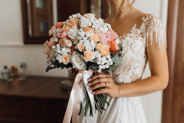 Bride holds the lush bouquet with delicate flowers colors