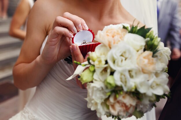 Bride holds red box with wedding rings in her arms