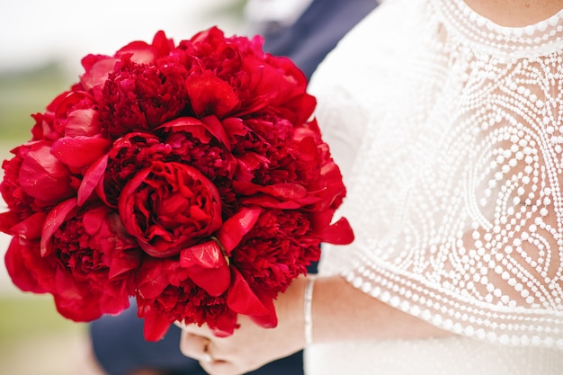 Bride holds rich wedding bouquet made of red peonies 