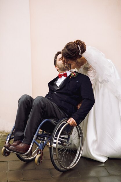 Невеста обнимает жениха на инвалидной коляске сзади позирует на улице