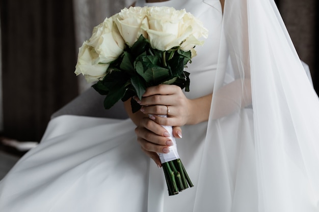 花嫁は彼女の手で上品な白いバラの花束を保持しています。