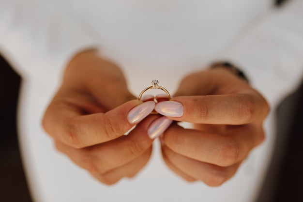 Невеста держит обручальное кольцо с бриллиантом в руках с красивым маникюром, вид спереди, день свадьбы
