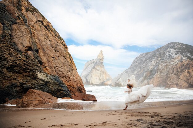 花嫁はビーチの岩の間で砂の上を実行しています
