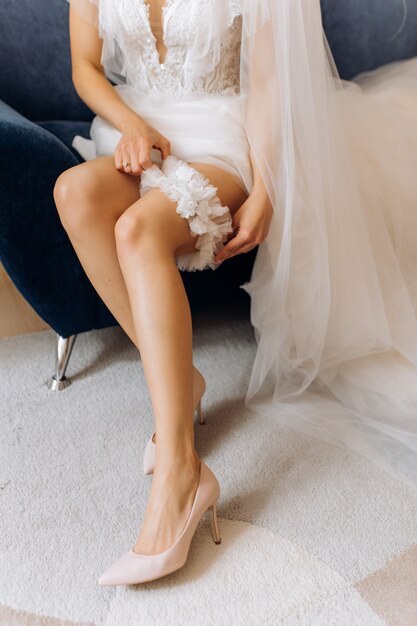 신부는 안락 의자에 앉아 그녀의 다리에 웨딩 양말을 착용