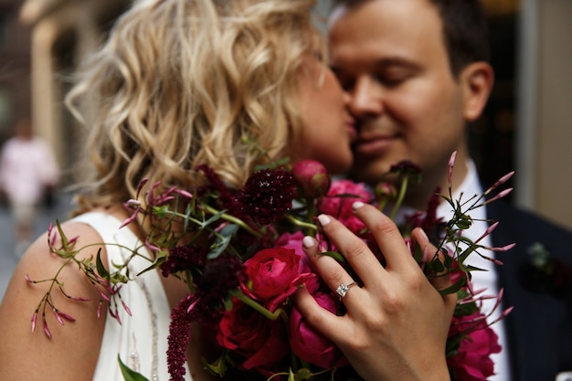 Bride kisses groom tender holding red wedding bouquet in her arms