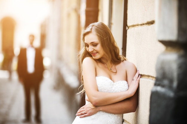 Bride leaning on wall and boyfriend behind defocused