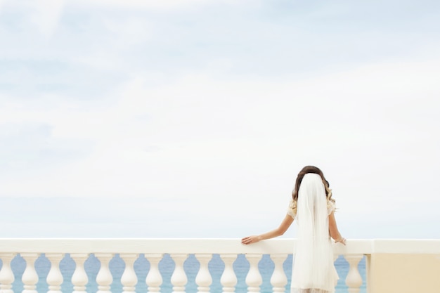 Free photo bride leans over a white balcony while admiring the sea