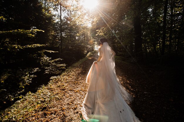 Bride in the long wedding dress goes on the forest path