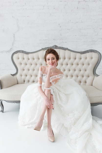 Bride looking out the window, she waits for the groom sitting on big classic sofa.