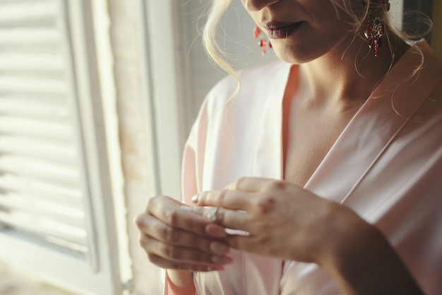 Bride in pink robe puts eing on her finger 