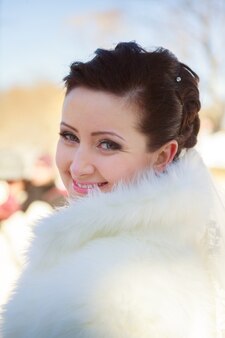 毛皮のコートで冬の森でポーズをとる花嫁。雪に覆われた公園での結婚式のフォトセッション。