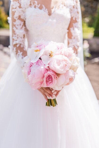 Bride in rich dress holds pink wedding bouquet of orchids and peonies