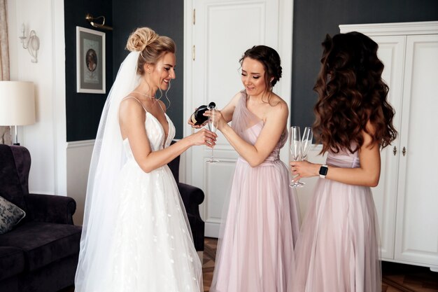 Bride's female friend is pouring the champagne to the bride and another woman