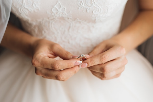 Bride's hands hold the beautiful engagement ring with gemstone, close up, without face