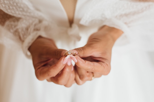 Bride's hands hold the minimalistic engagement ring with gemstone, close up, without face