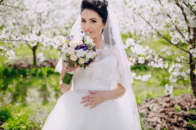 花嫁は、開花の木の背景と彼女の花束を嗅ぎます