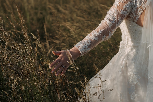 Foto gratuita sposa che cammina in un campo di grano che indossa un bellissimo abito da sposa e un braccialetto di perle