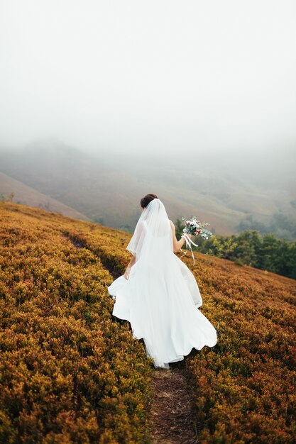 Bride walks on a hill covered with smoke