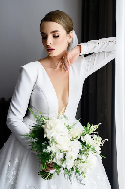 Невеста в свадебном платье с букетом позирует в помещении