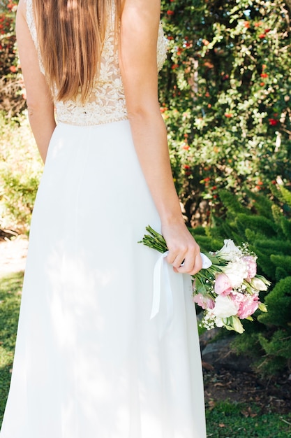 Невеста в белом платье, держа в руке букет цветов