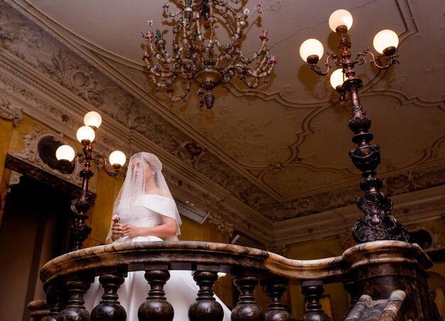 Bride With Closing Face Of Veil Standing On Balcony In Vitage Castle