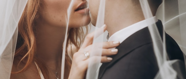 Bride with red hair kisses groom standing under the veil