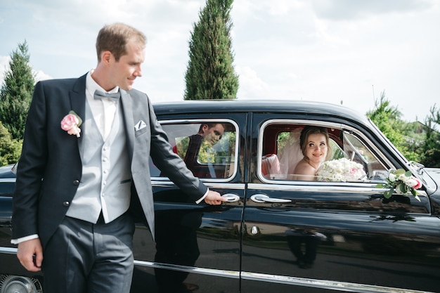 Foto gratuita lo sposo è in piedi accanto alla macchina mentre la sposa è in macchina