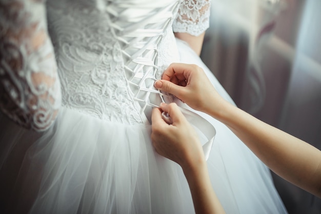 Бесплатное фото bridesmaid делает bow-knot на задней части свадебного платья невест