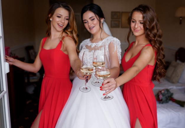 Foto gratuita le damigelle in abiti rossi bevono vino con la sposa nella stanza