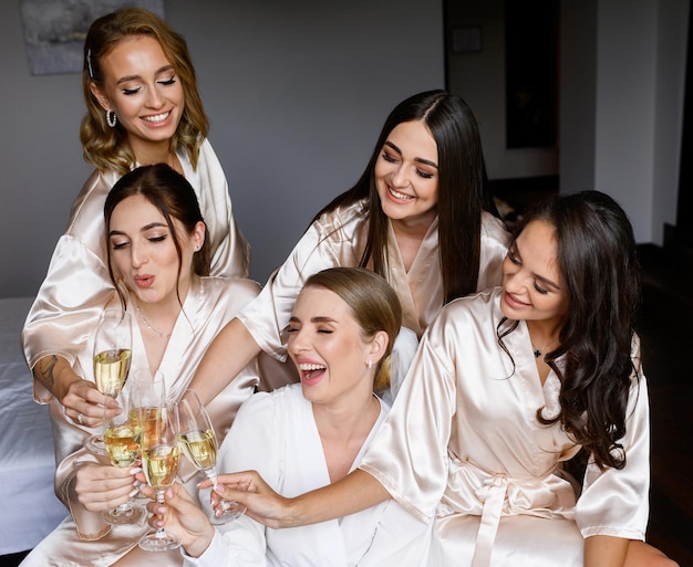 Подружки невесты и невеста чокаются стаканами с напитком в помещении