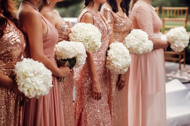 ピンクのドレスのブライドメイドは、白い花の花束と一緒に立つ