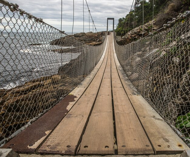 Bridge made of wood and metal going around the mountain next to the beach