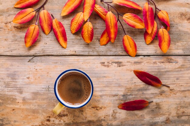 木製の背景に明るい紅葉とコーヒーのカップ