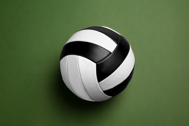 Bright black and white volleyball ball. Professional sport equipment isolated on green studio background.