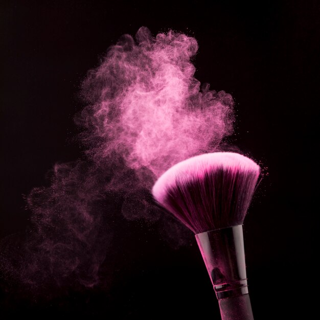 Bright dust of powder and brush for makeup on black background