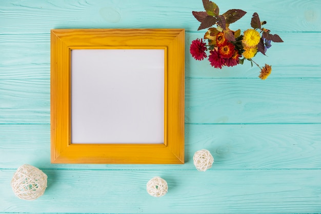 Free photo bright flowers near blank frame on wooden table