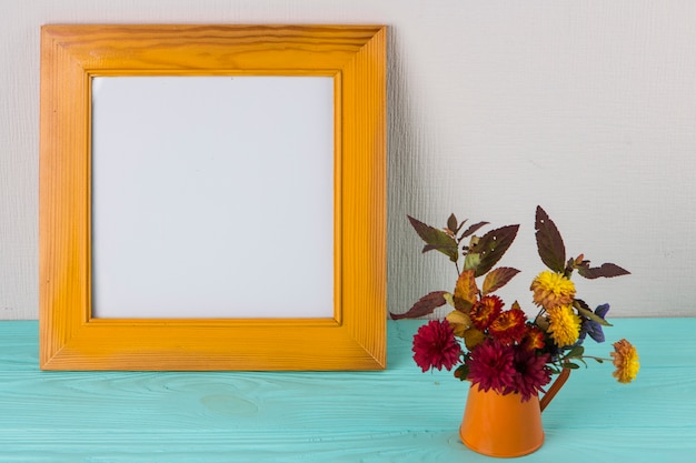 Bright flowers in vase near frame on table