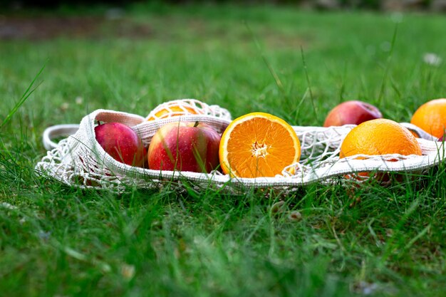 Bright fruits in a white string bag in the grass