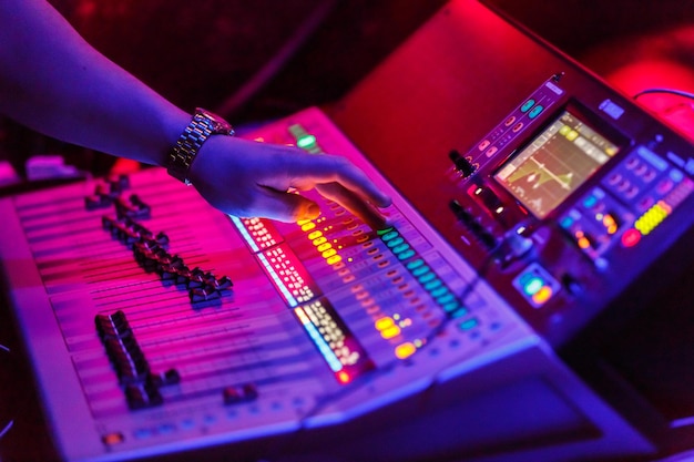 Яркое изображение рук звукорежиссера, работающего с концертным звуковым оборудованием - музыкальной консолью для микширования звука с кнопками с подсветкой. звук, музыкальное оборудование и концепция технологий
