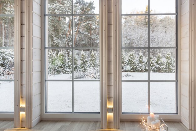 冬​の​中庭​を​見下ろす​大きな​窓​の​ある​木造​住宅​の​部屋​の​明るい​インテリア​。​白い​窓​の​雪​の​冬​の​風景​。​家​と​庭​、​クリスマス​の​コンセプト​。
